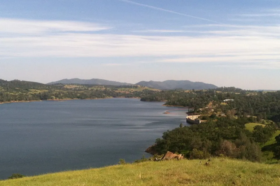 A large reservoir and its dam are shown in golden foothills.